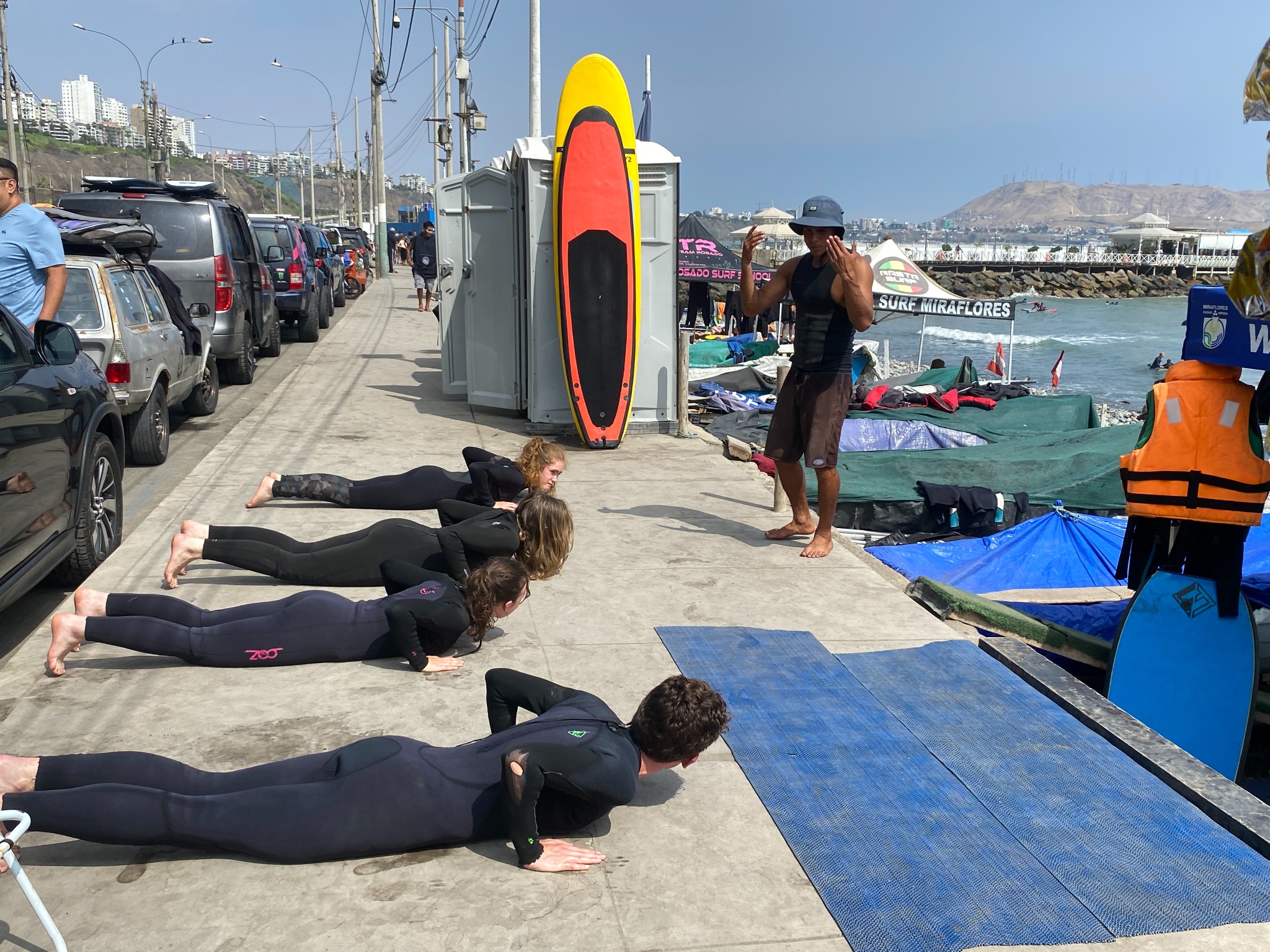 Instructor leading a warm-up beside the sea with students and surfboards